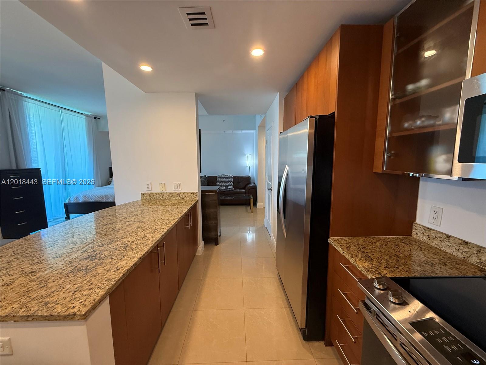 A kitchen with granite countertops, wood cabinets, and stainless steel appliances leads to a living area — 1945 S Ocean Dr # 312, Hallandale Beach FL 33009, HALLANDALE BEACH, FL