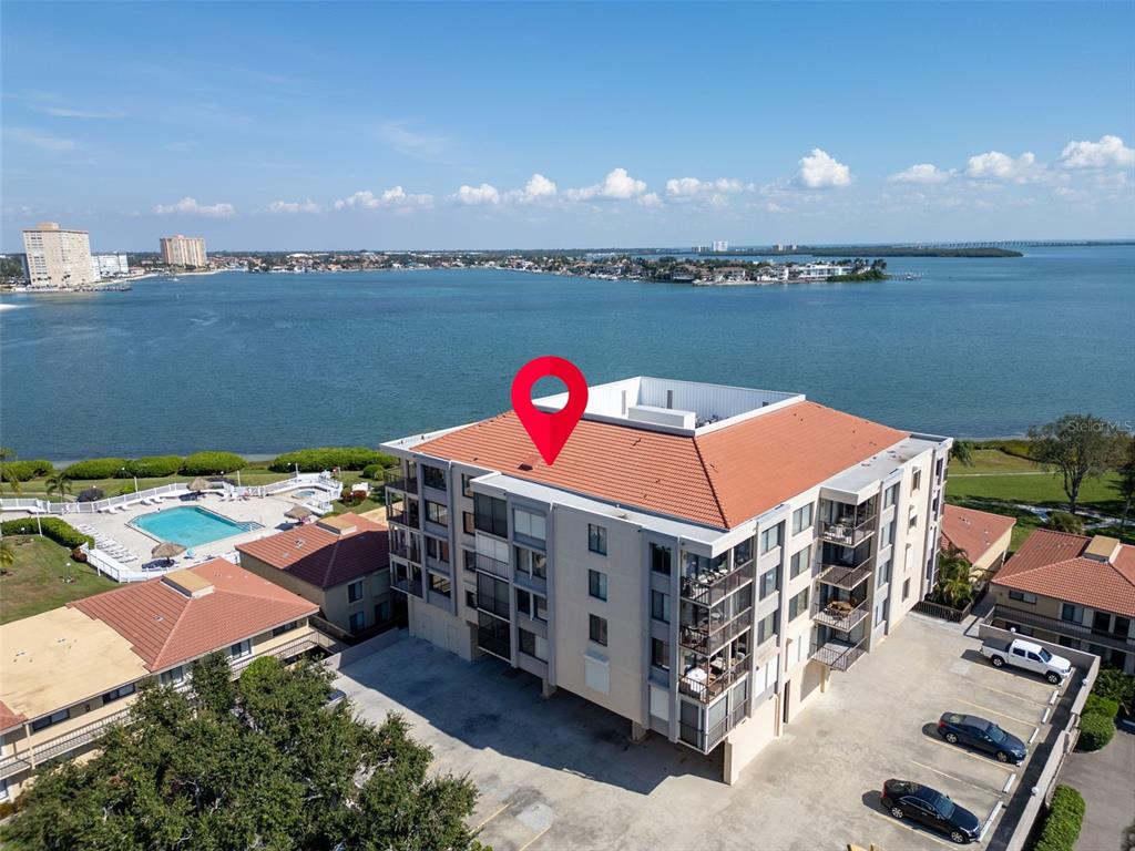 An aerial view shows a multi-story apartment building with a red tile roof near water — 6158 PALMA DEL MAR SO UNIT 505, ST PETERSBURG, FL