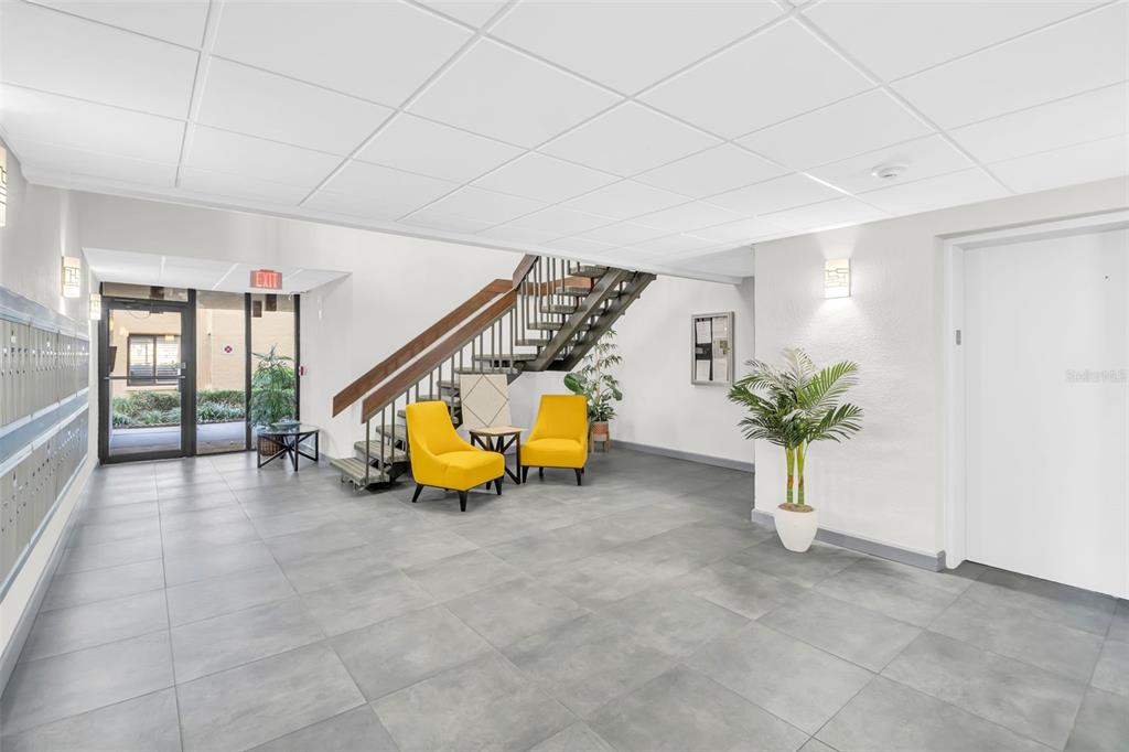 A lobby features gray tile flooring, two yellow chairs, a staircase, and a potted plant — 6158 PALMA DEL MAR SO UNIT 505, ST PETERSBURG, FL