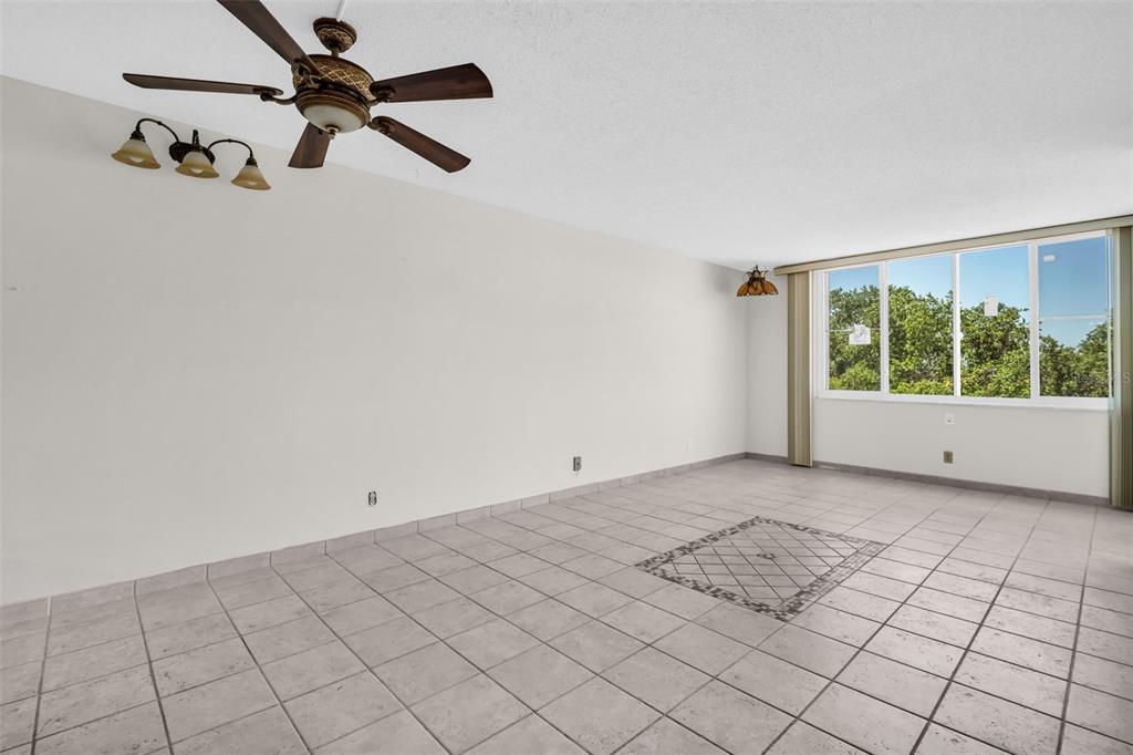 An empty room with light-colored tile flooring, a ceiling fan, and a large window — 6158 PALMA DEL MAR SO UNIT 505, ST PETERSBURG, FL