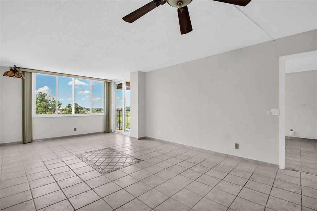 An empty living room features light-colored tile flooring, a ceiling fan, and large windows — 6158 PALMA DEL MAR SO UNIT 505, ST PETERSBURG, FL