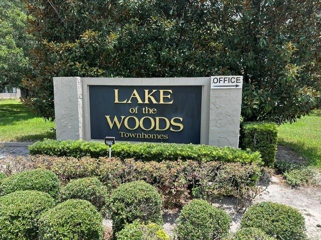 A sign for Lake of the Woods Townhomes stands in front of a large bush — 805 WESTWIND LANE, FERN PARK, FL