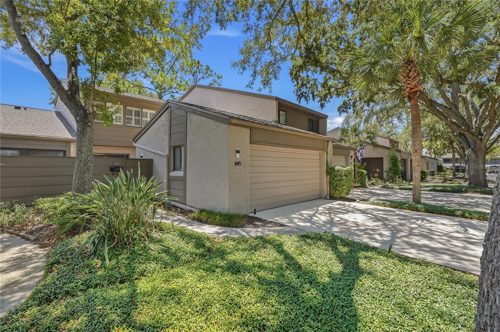 A tan townhouse exterior features a single-car garage, a concrete driveway, and surrounding landscaping — 805 WESTWIND LANE, FERN PARK, FL