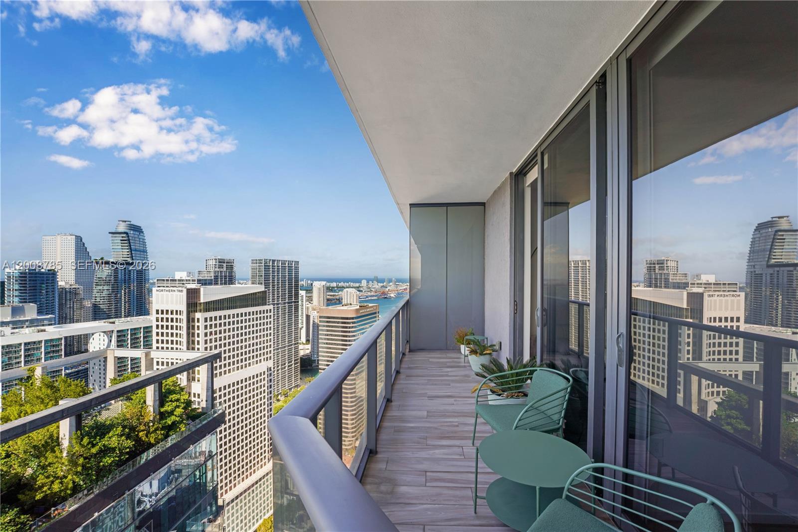 A high-rise balcony with wood-look tile flooring, metal furniture, and views of a city skyline — 801 S Miami Ave # 5206, Miami FL 33130, MIAMI, FL