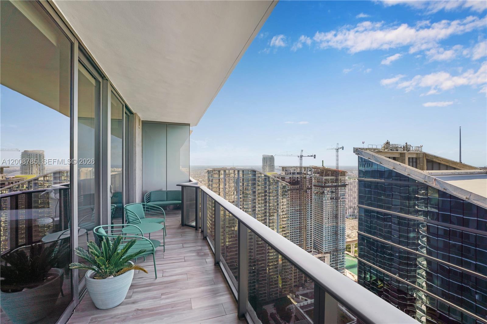 A high-rise balcony features teal metal furniture, a potted plant, and city skyline views — 801 S Miami Ave # 5206, Miami FL 33130, MIAMI, FL