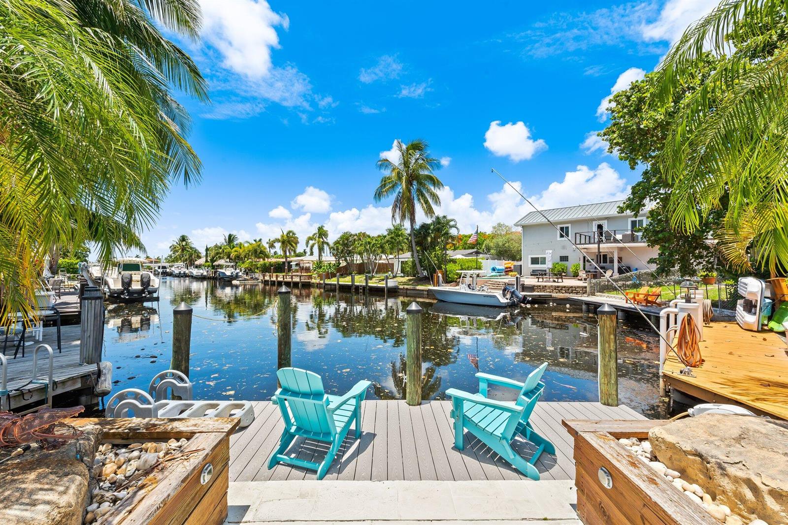 Two turquoise chairs sit on a wooden dock overlooking a canal with boats and palm trees — 581 SE 5th Avenue, Pompano Beach FL 33060, POMPANO BEACH, FL