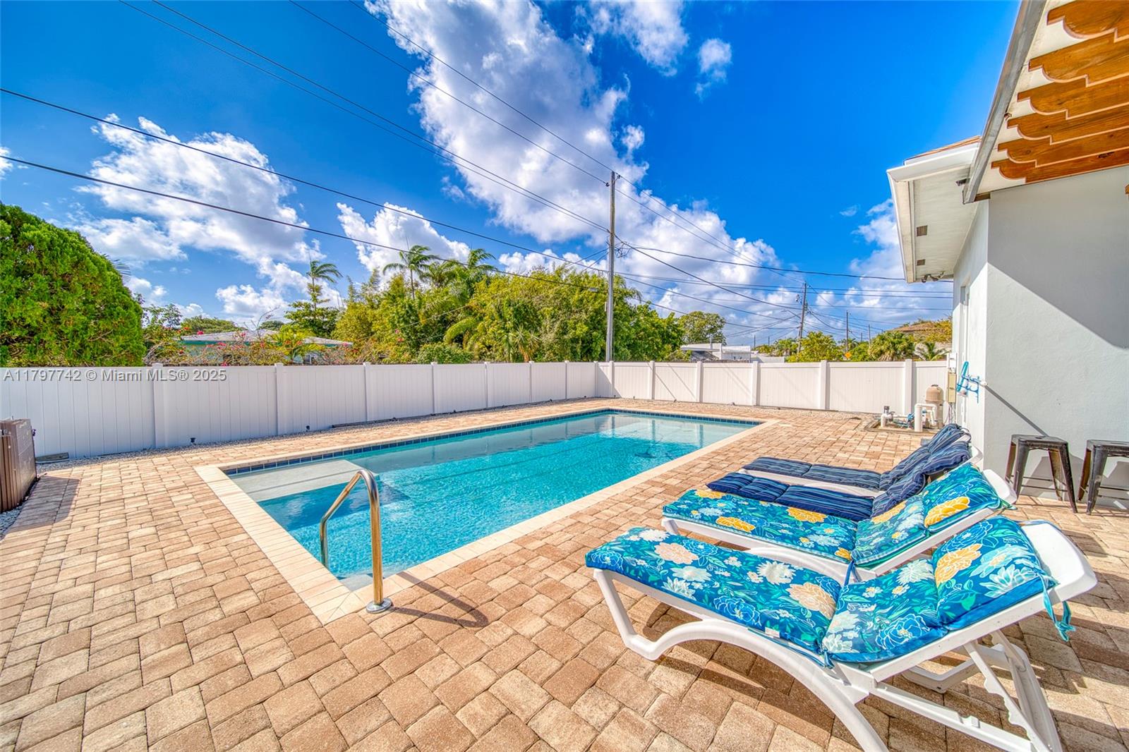 A rectangular swimming pool with a patio and lounge chairs sits in a fenced backyard — 207 SW 11th St, Dania Beach FL 33004, DANIA BEACH, FL