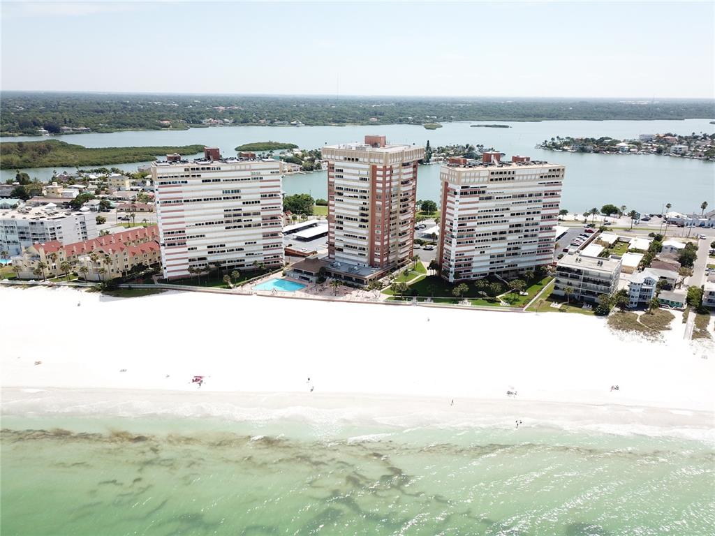 An aerial view shows three high-rise residential buildings situated along a sandy beach and water — 17940 GULF BOULEVARD UNIT 6E, REDINGTON SHORES, FL