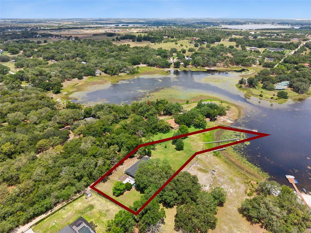 An aerial view shows a house on a large, grassy lot bordering a lake — 3421 REX DRIVE, WINTER GARDEN, FL
