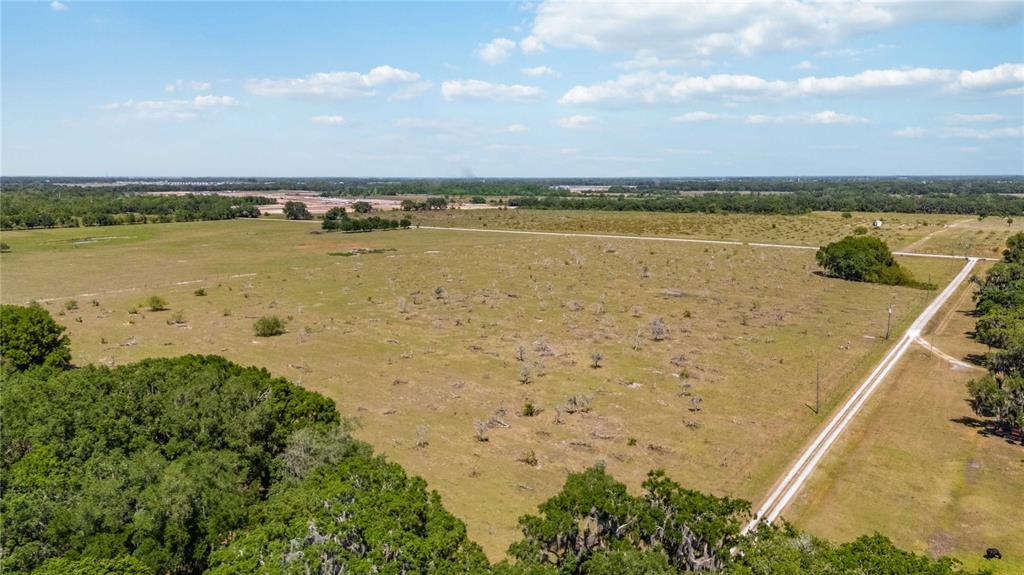 An aerial view shows a large, open grassy field with scattered trees and a dirt road — 0 LAKE TOHOPEKALIGA ROAD, ST CLOUD, FL