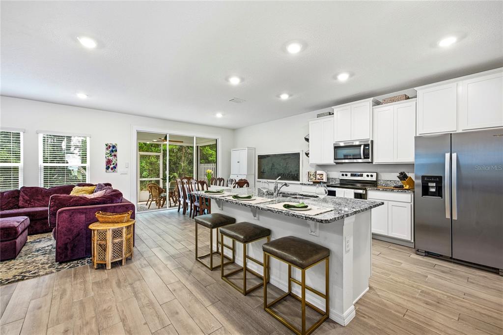A kitchen with white cabinets and granite countertops opens to a living area with flooring — 1197 NW 133RD WAY, NEWBERRY, FL