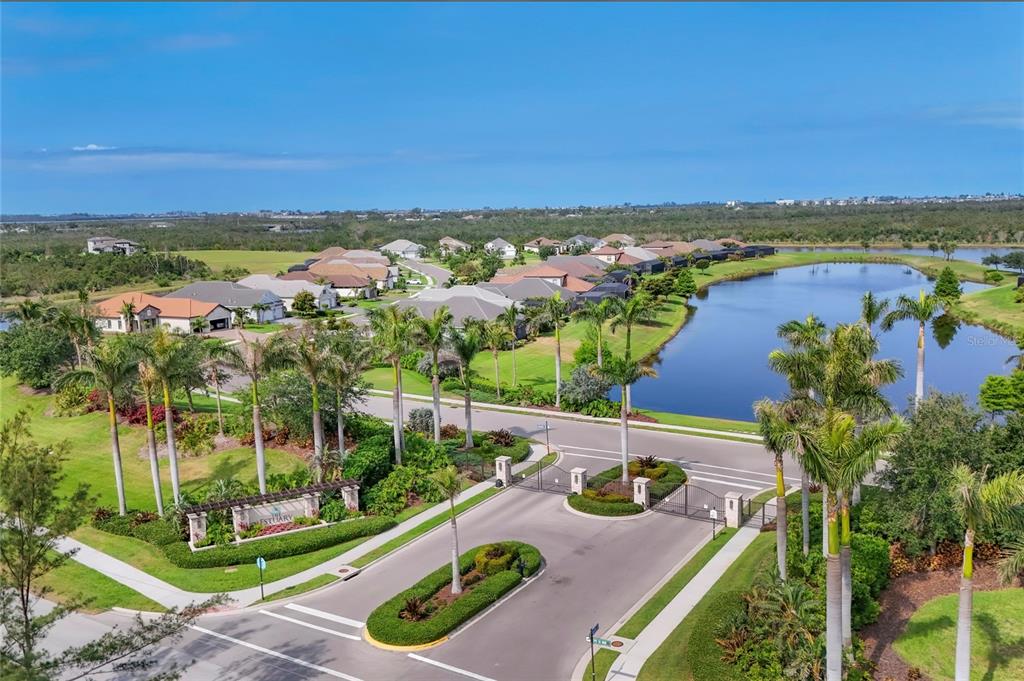 An aerial view shows a gated residential community entrance with palm trees and a lake — 519 WILDLIFE GLEN, BRADENTON, FL