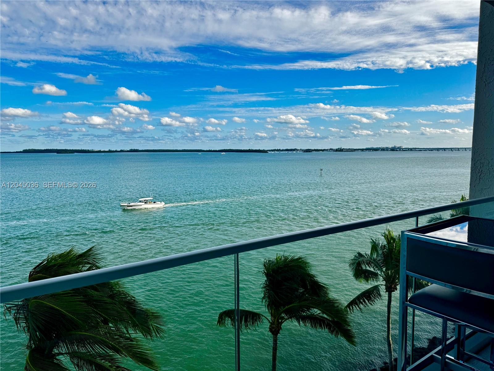 A balcony overlooks a wide body of water with a boat and palm trees — 800 Claughton Island Dr # 502, Miami FL 33131, MIAMI, FL