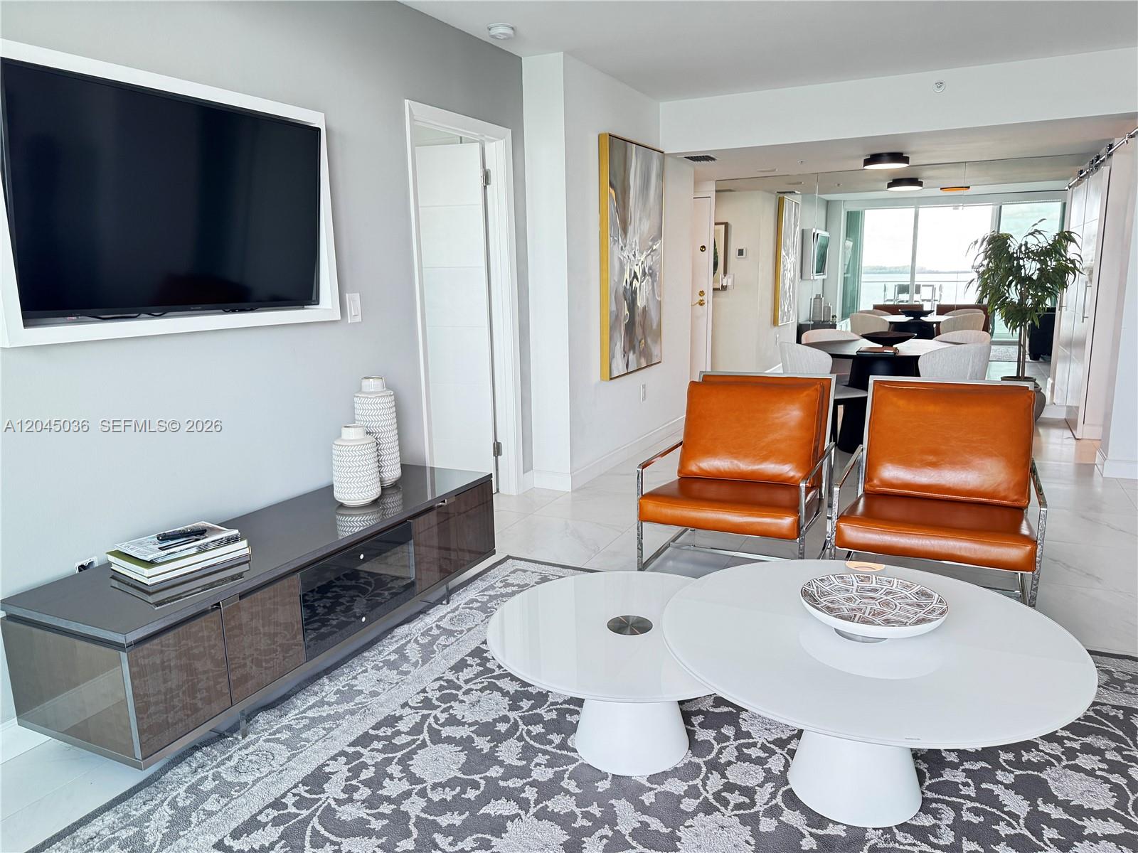A modern living room features two orange leather chairs, white coffee tables, and a television — 800 Claughton Island Dr # 502, Miami FL 33131, MIAMI, FL