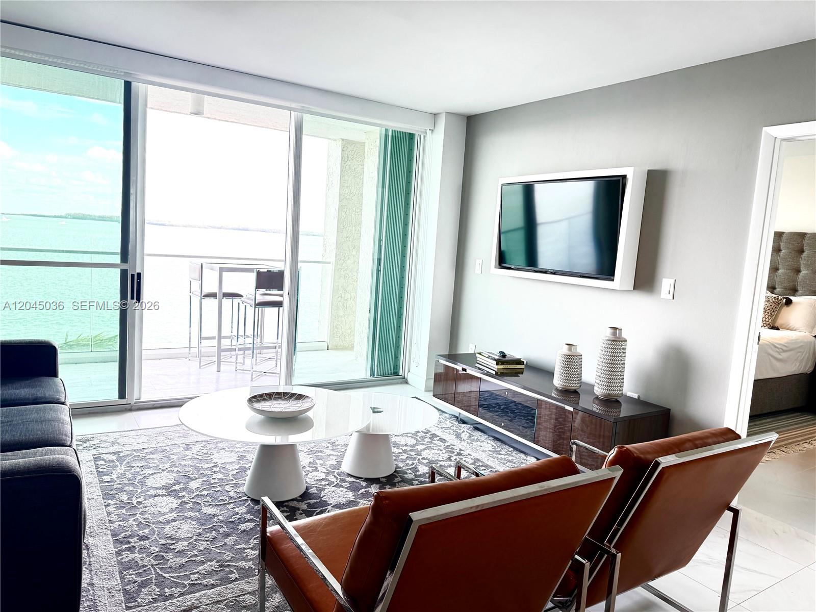 A living room features a television, two leather chairs, a coffee table, and balcony access — 800 Claughton Island Dr # 502, Miami FL 33131, MIAMI, FL