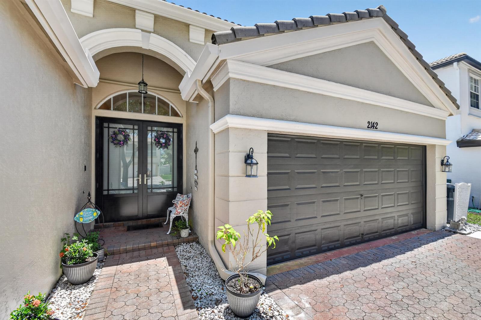 The exterior of a house features a dark garage door, double front doors, and pavers — 2142 Balsan Way, Wellington FL 33414, WELLINGTON, FL