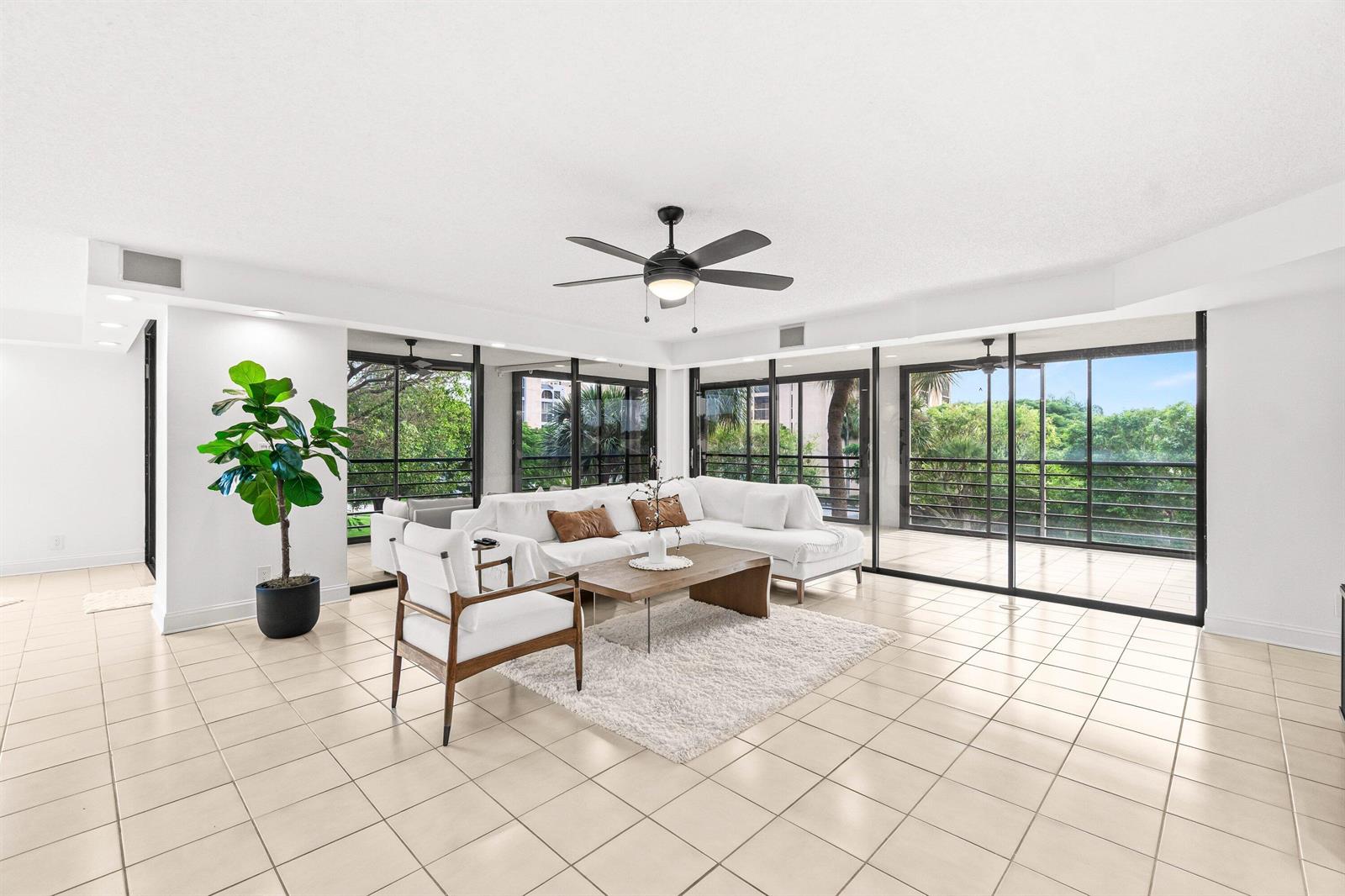 A bright living room features white tile floors, a sectional sofa, and floor-to-ceiling glass doors — 7201 Promenade Drive E # 302, Boca Raton FL 33433, BOCA RATON, FL