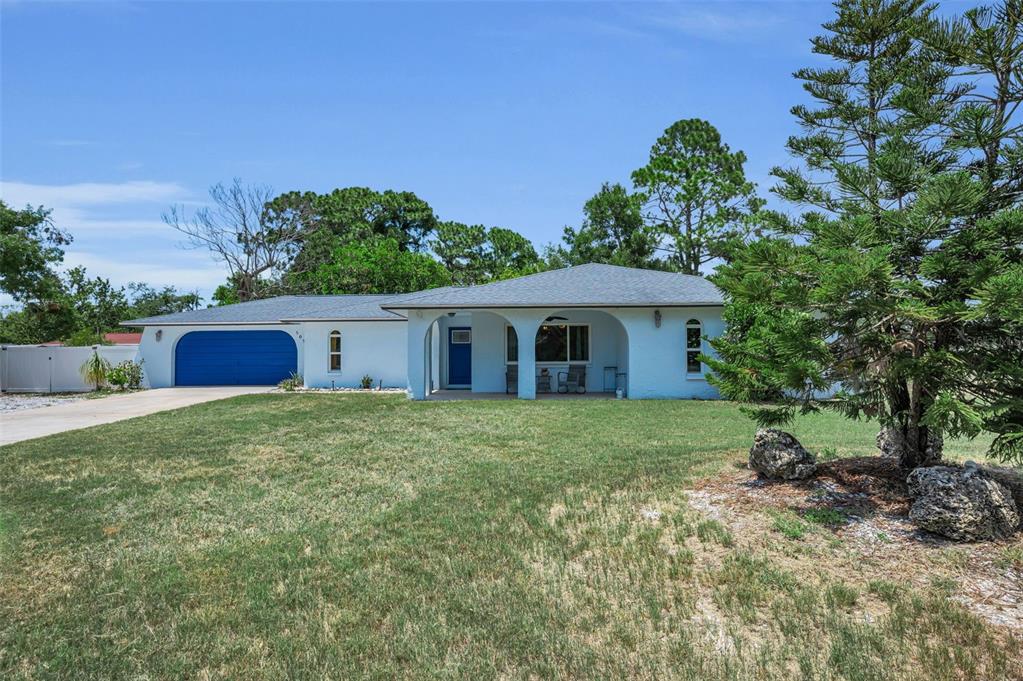 A single-story white house with a blue garage door and a covered front porch — 505 WHISPERING OAK DRIVE, TARPON SPRINGS, FL