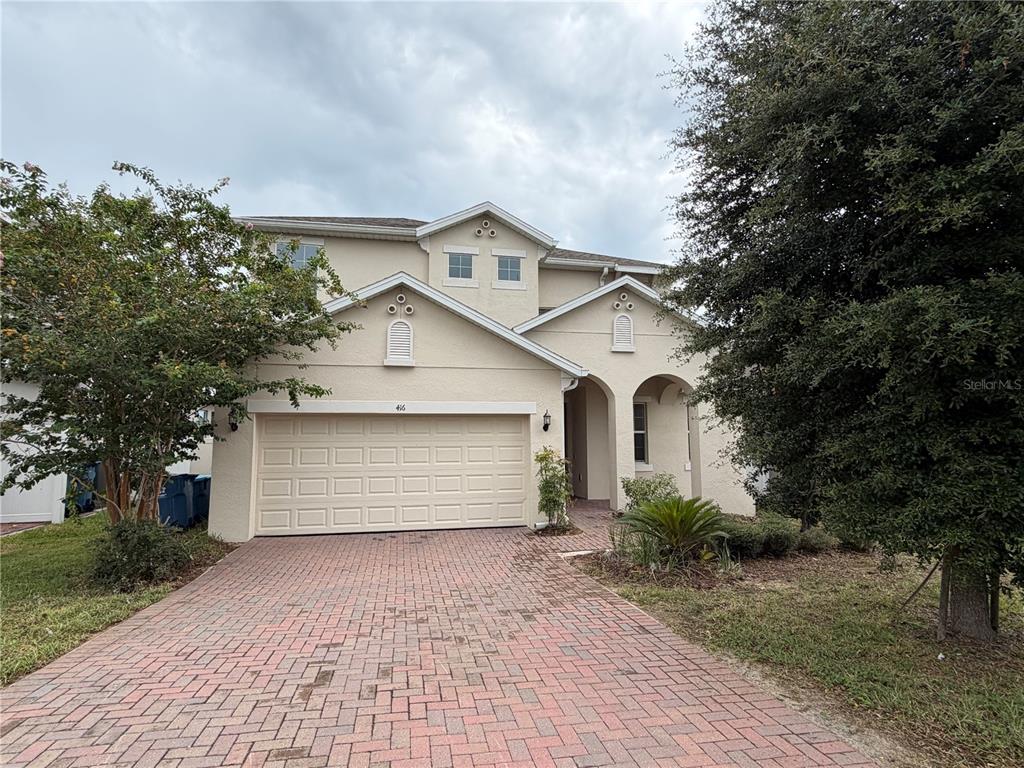 A two-story house with a beige stucco exterior, a brick driveway, and a two-car garage — 416 SAPPHIRE DR, DAVENPORT, FL