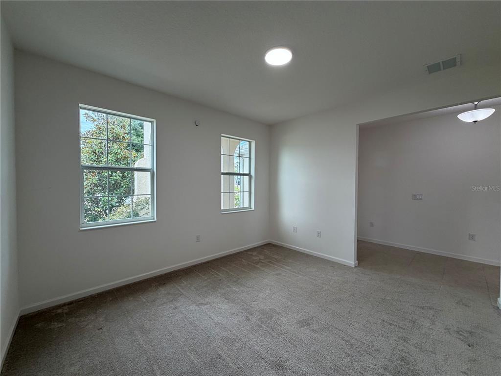 An empty room with beige carpet, white walls, two windows, and an adjacent tiled area — 416 SAPPHIRE DR, DAVENPORT, FL