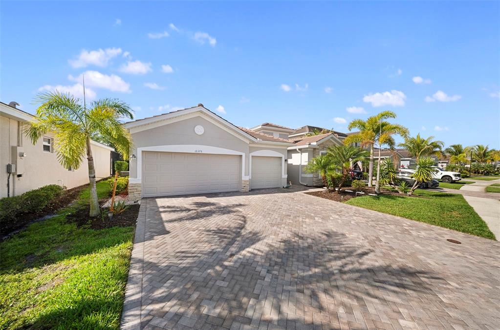 A beige house with a three-car garage and a paved driveway under a blue sky — 16378 BONITA LANDING CIRCLE, BONITA SPRINGS, FL