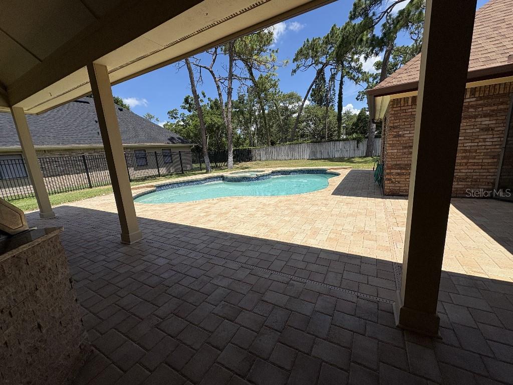 A covered brick patio overlooks a swimming pool in a fenced backyard — 10484 LONGWOOD DRIVE, SEMINOLE, FL