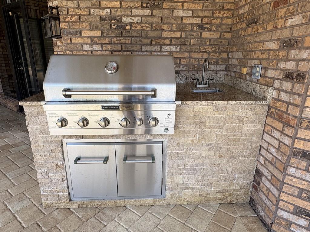 An outdoor kitchen features a stainless steel KitchenAid grill, a small sink, and stone masonry — 10484 LONGWOOD DRIVE, SEMINOLE, FL
