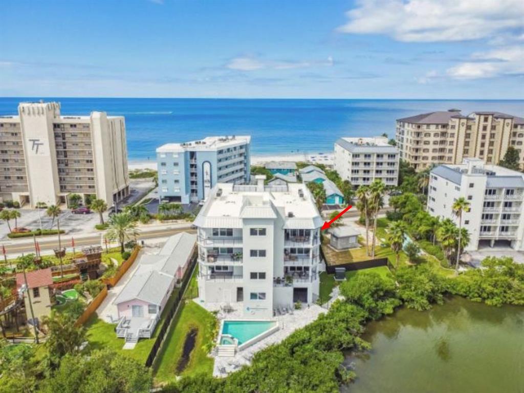 An aerial view of a multi-story coastal condominium building with a pool and nearby beach — 19505 GULF BOULEVARD UNIT 404, INDIAN SHORES, FL