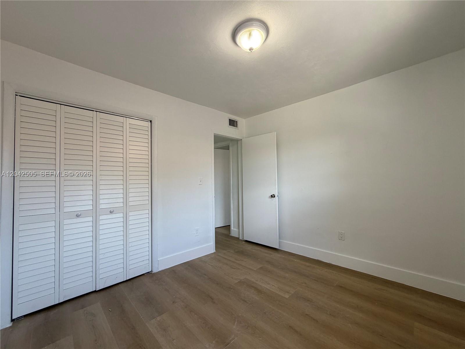 A bedroom features white walls, light wood-look flooring, a white louvered closet, and a doorway — 1021 NW 5th St # 6, Miami FL 33128, MIAMI, FL