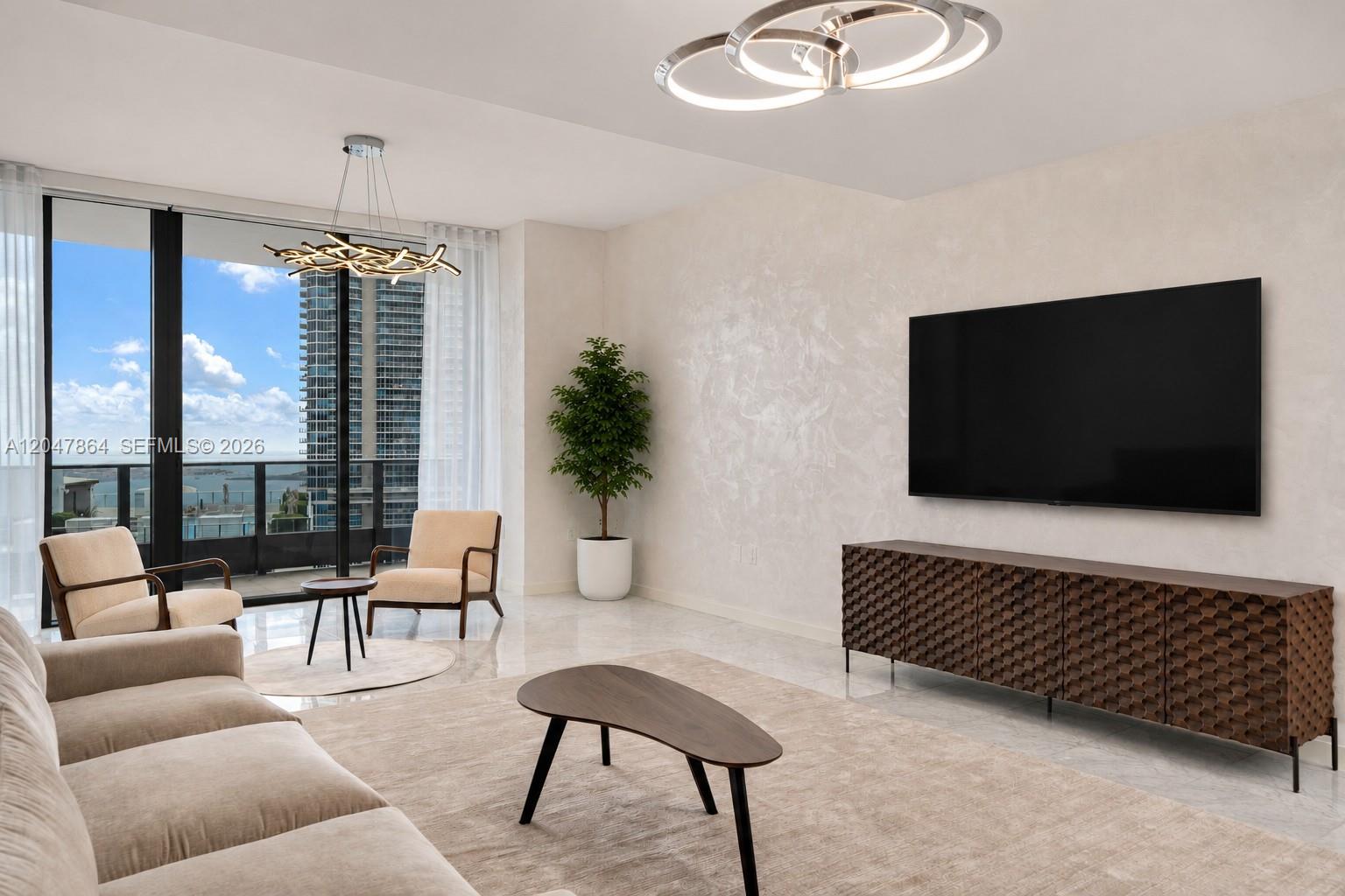 A modern living room features a wall-mounted television, textured walls, and floor-to-ceiling windows — 1000 Brickell Plz, Miami FL 33131, MIAMI, FL