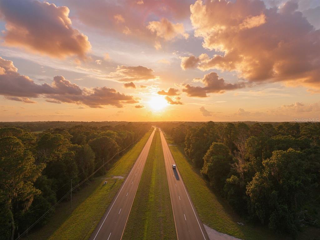 An aerial view shows a straight road stretching through a forest toward a sunset sky — 24368 DORSEY SMITH ROAD, BROOKSVILLE, FL