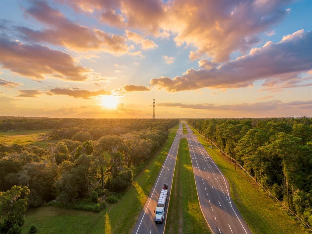 An aerial view shows a highway stretching through a forested landscape during a sunset — 24368 DORSEY SMITH ROAD, BROOKSVILLE, FL