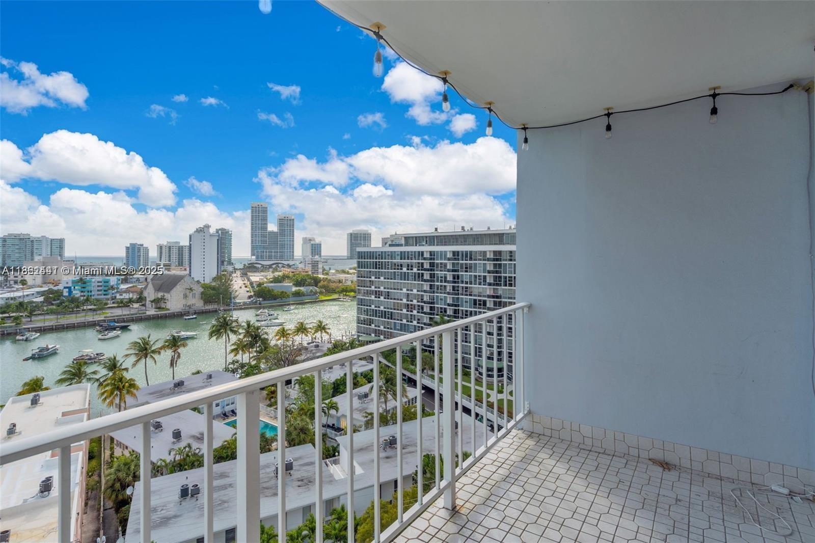 A balcony with white railings overlooks a waterway, palm trees, and a city skyline — 6900 Bay Dr # 11F, Miami Beach FL 33141, MIAMI BEACH, FL