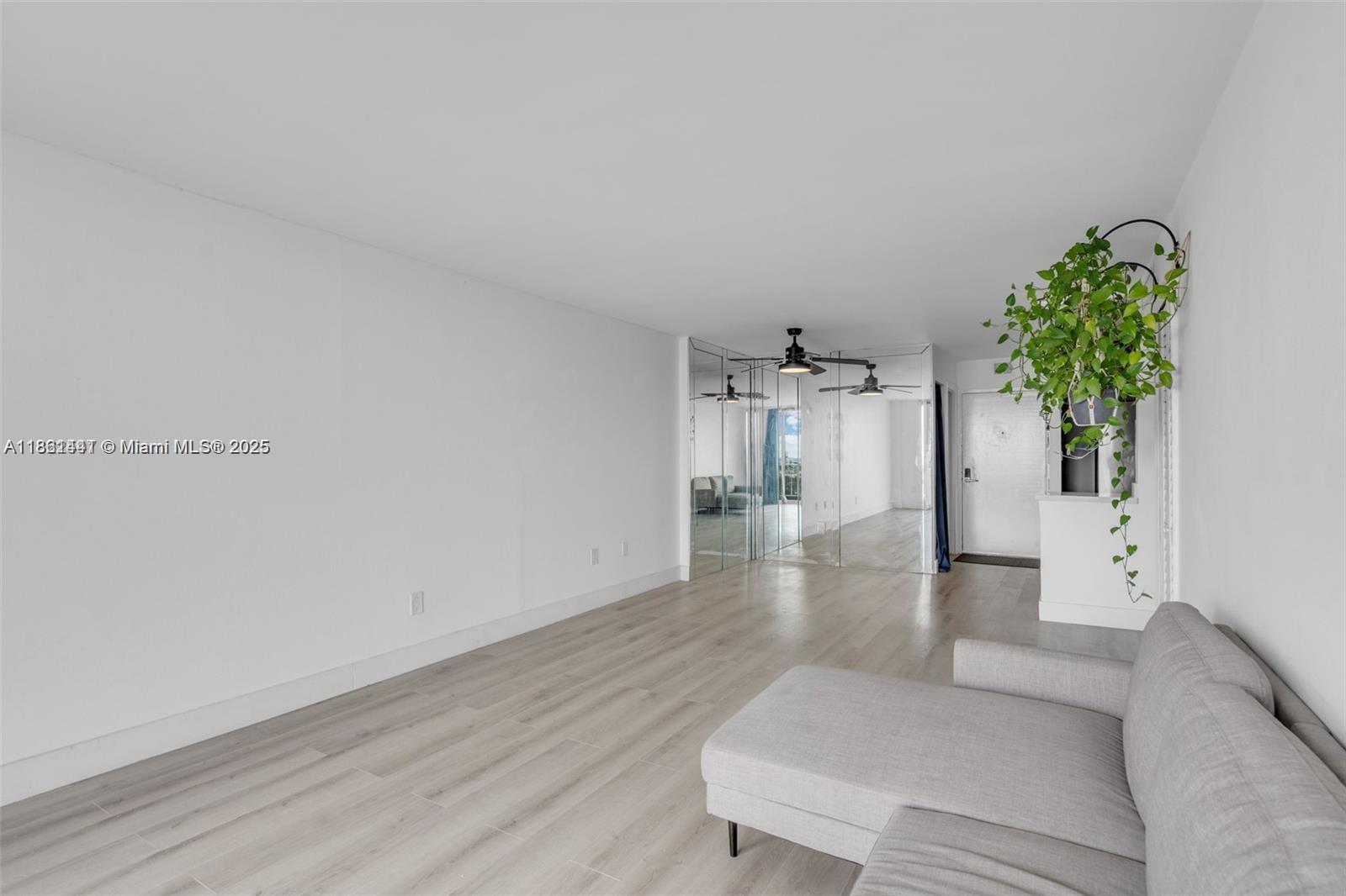 A living room features light wood-look flooring, a grey sectional sofa, and mirrored wall panels — 6900 Bay Dr # 11F, Miami Beach FL 33141, MIAMI BEACH, FL