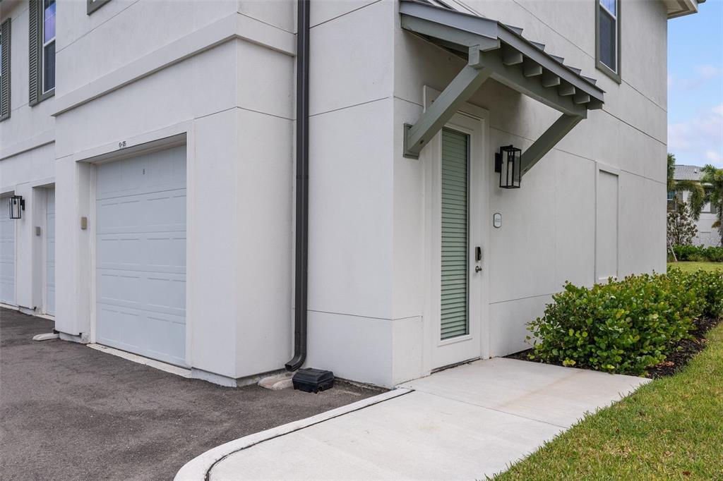 A white exterior wall features a garage door, a side entrance door, and landscaping — 1700 RANCH ROAD UNIT B4-8202, NOKOMIS, FL