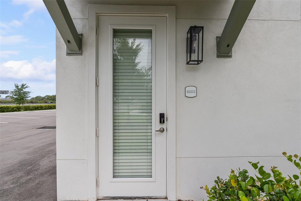 A white exterior door with a glass insert and blinds sits beside a wall-mounted light — 1700 RANCH ROAD UNIT B4-8202, NOKOMIS, FL