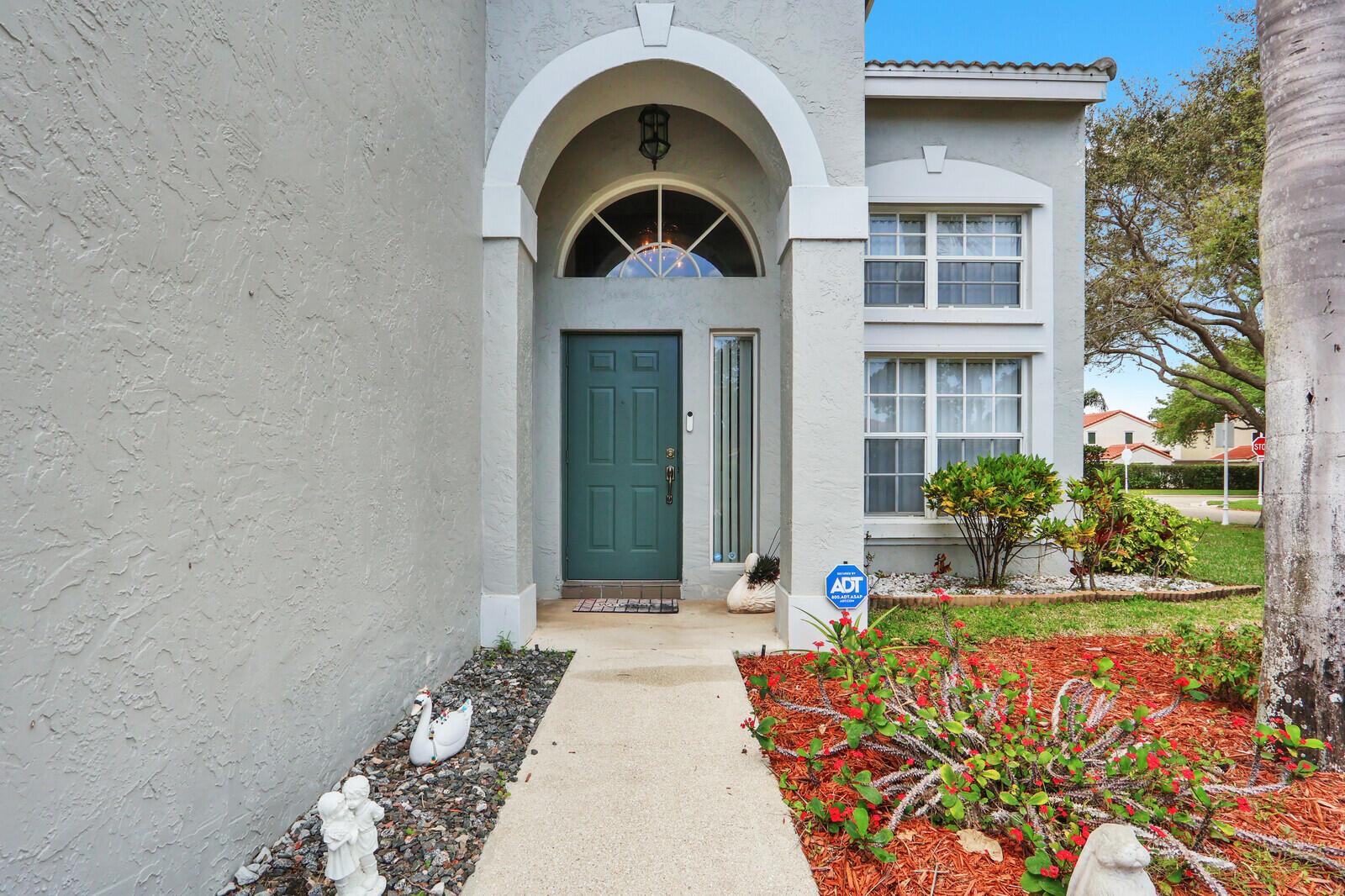 A gray house exterior features a teal front door, arched entryway, and landscaped front yard — 8156 Mystic Harbor Circle, Boynton Beach FL 33436, BOYNTON BEACH, FL