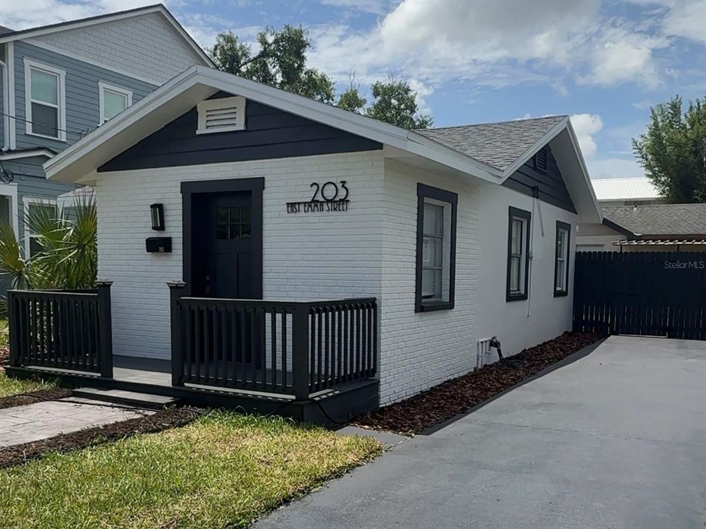 A small white house with a dark trim and a paved driveway sits beside a larger home — 203 E EMMA STREET, TAMPA, FL