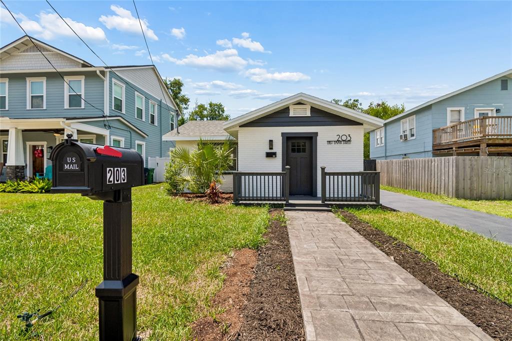 A small white house with a dark front door and porch sits behind a paved walkway — 203 E EMMA STREET, TAMPA, FL