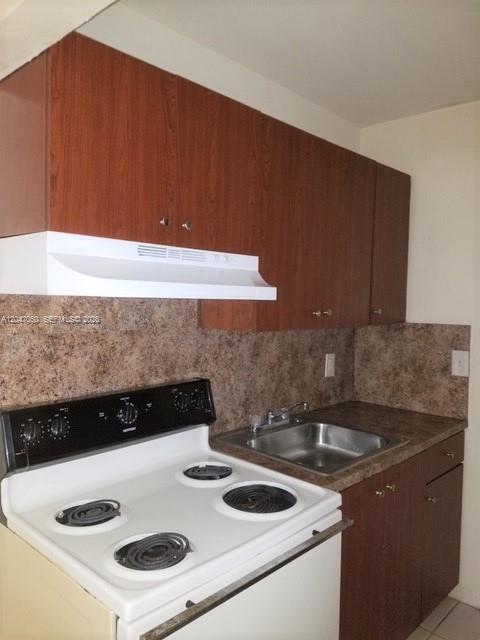 A kitchen features wood-toned cabinets, a white electric stove, and a stainless steel sink — 2230 Madison St # 14, Hollywood FL 33020, HOLLYWOOD, FL