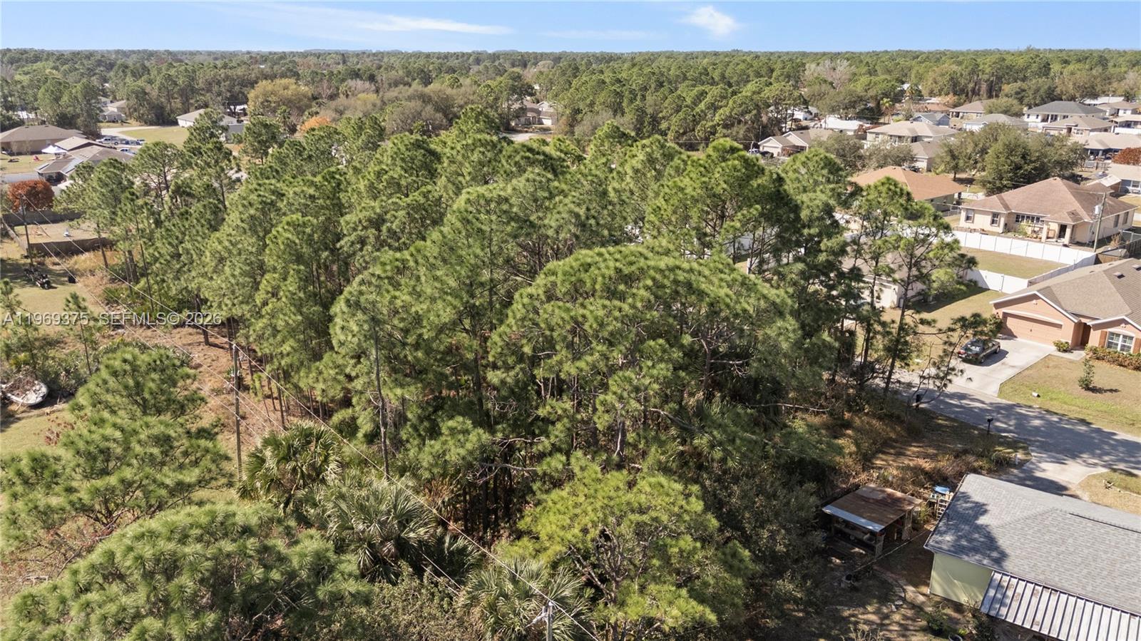 An aerial view shows a wooded lot surrounded by residential houses and a paved street — 985 Cranberry Rd SE, Palm Bay FL 32909, PALM BAY, FL
