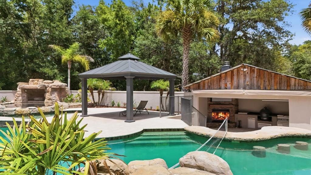 A backyard swimming pool features a gazebo, outdoor kitchen, fireplace, and a swim-up bar — 91 S SCHOOL AVENUE, LECANTO, FL
