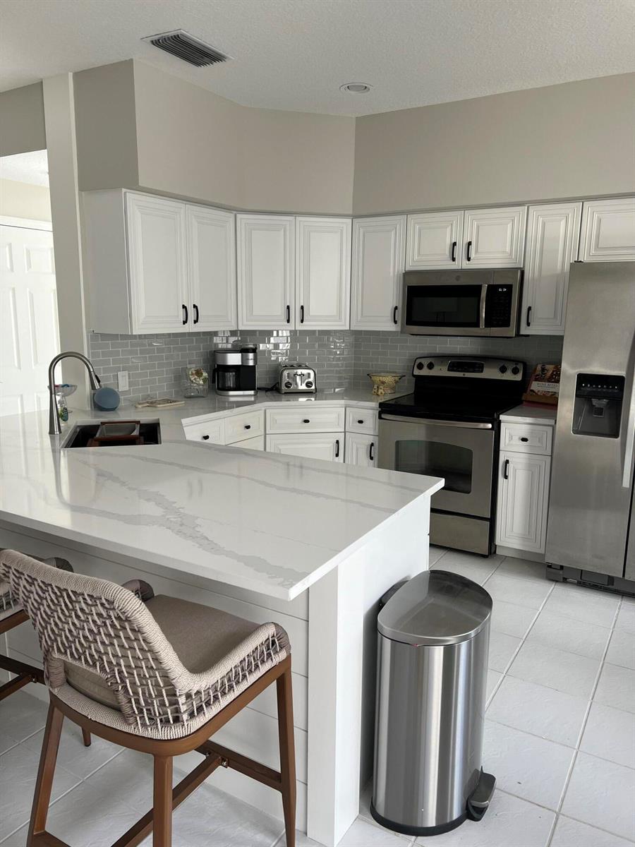 A kitchen features white cabinets, quartz countertops, stainless steel appliances, and a gray subway tile backsplash — 3028 Windward Way, Jupiter FL 33477, JUPITER, FL