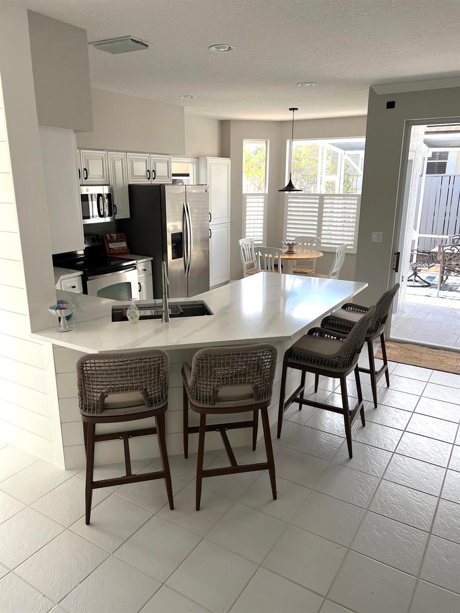 A kitchen with white cabinets, a quartz island, bar stools, and a view of a patio — 3028 Windward Way, Jupiter FL 33477, JUPITER, FL