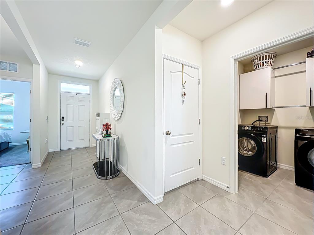 A tiled entryway features a white front door, a laundry closet, and a decorative mirror — 1737 AURORA RIDGE DRIVE, ZELLWOOD, FL