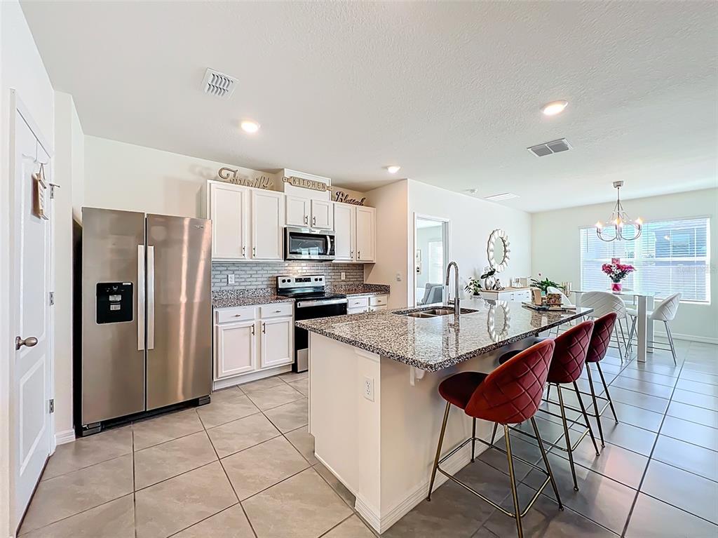 A kitchen features white cabinets, granite countertops, stainless steel appliances, and a central island — 1737 AURORA RIDGE DRIVE, ZELLWOOD, FL