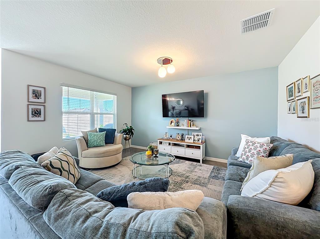 A living room features a blue accent wall, a sectional sofa, and a television — 1737 AURORA RIDGE DRIVE, ZELLWOOD, FL