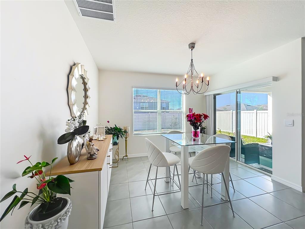 A dining room with a glass table, white chairs, a sideboard, and sliding glass doors — 1737 AURORA RIDGE DRIVE, ZELLWOOD, FL