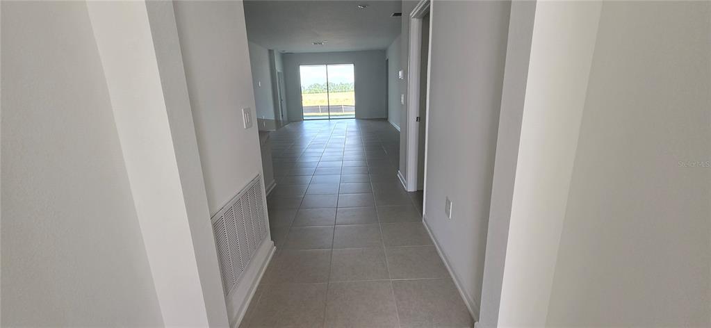 A hallway with light-colored tile flooring leads toward an open living area with sliding doors — 2451 BLUESTONE ROAD, LAKE HAMILTON, FL