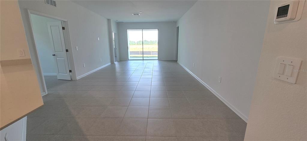 A bright, empty living room with light-colored tile flooring and a sliding glass door — 2451 BLUESTONE ROAD, LAKE HAMILTON, FL